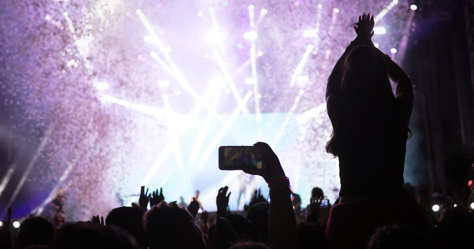 Crowd cheering with raised phones and confetti under bright lights at a Bad Bunny Grammy concert moment.