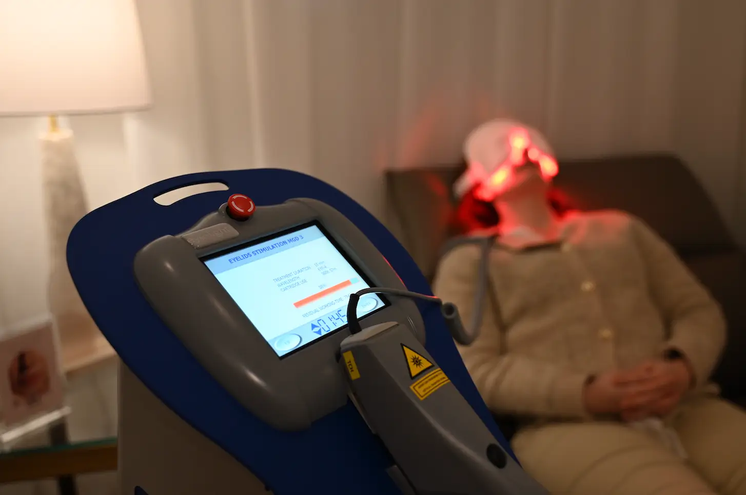 Woman reclining with LED eye mask during low level light therapy for eyes in a calm clinic setting.